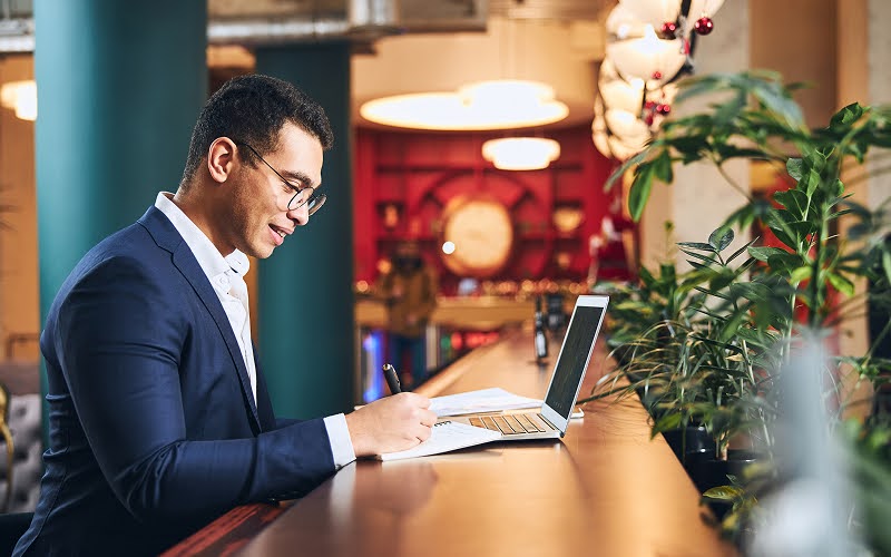 A businessman working on a laptop and taking notes in a hotel lounge.