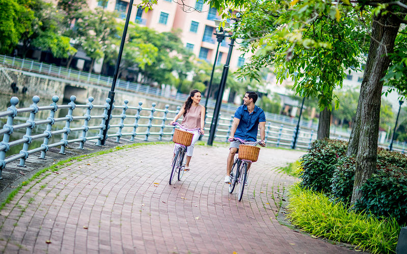 Couple cycling along Robertson Quay river during slow travel vacation.